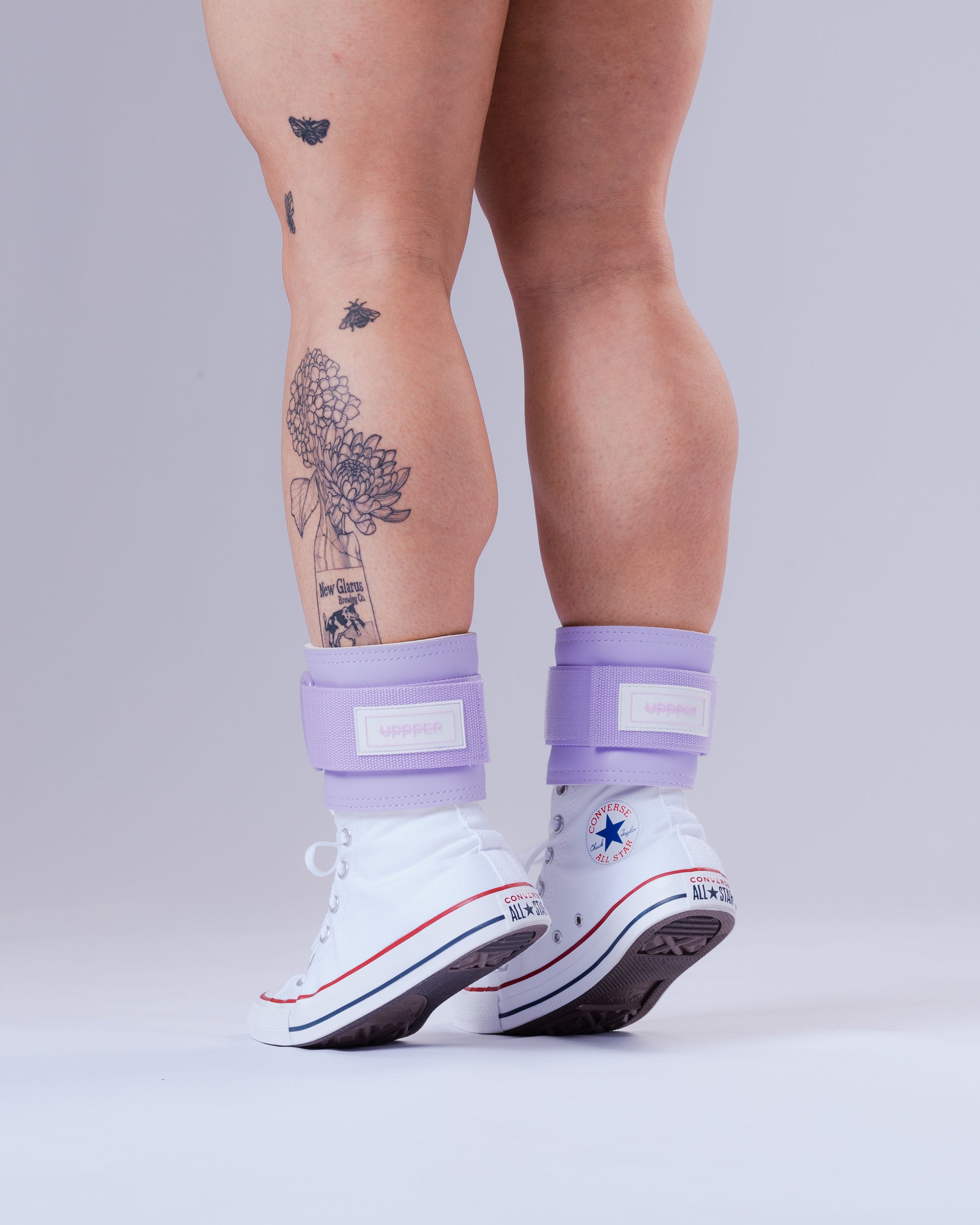person wearing white sneakers with purple uppper ankle weights on a light gray background