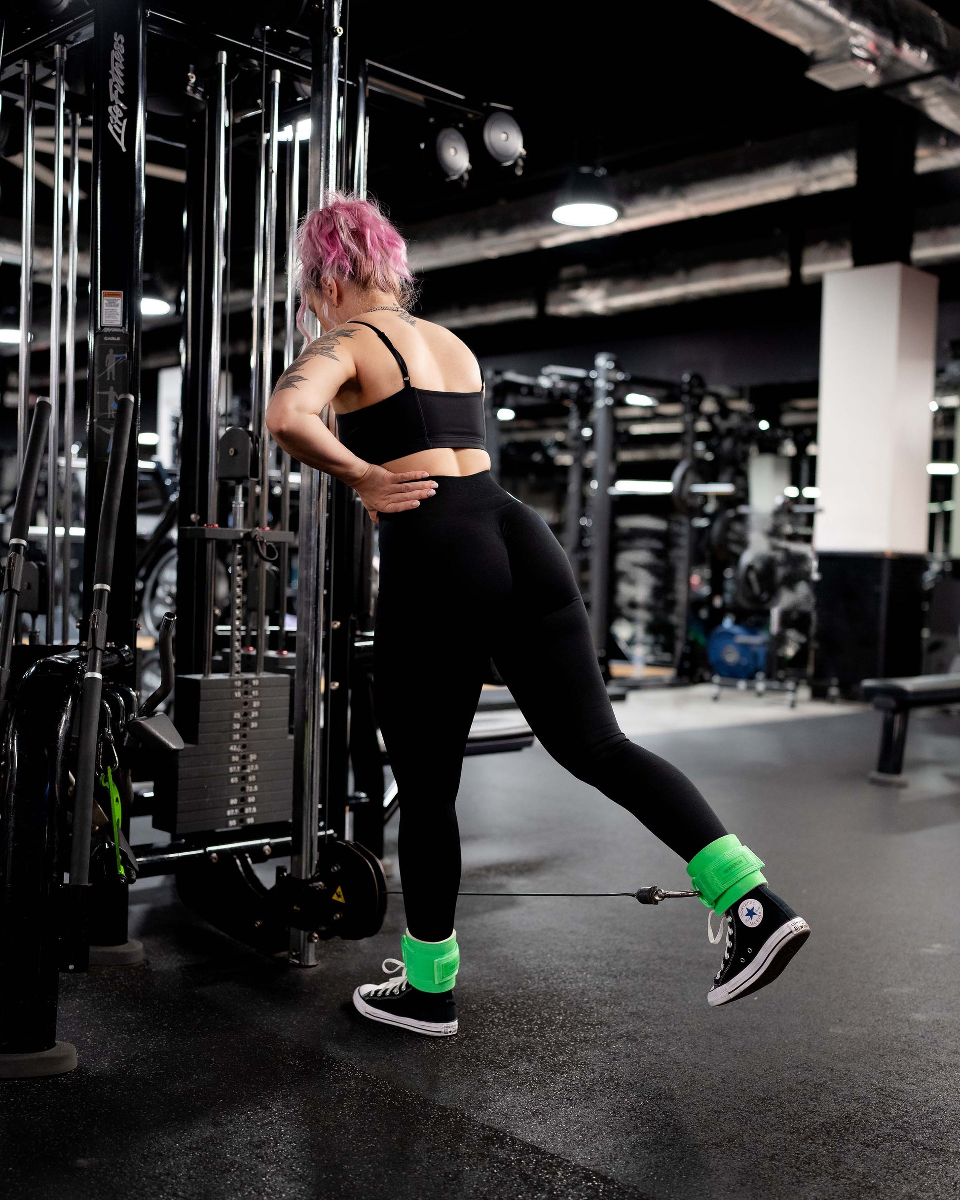 athlete exercising on cable machine using neon green uppper ankle straps in a gym setting 