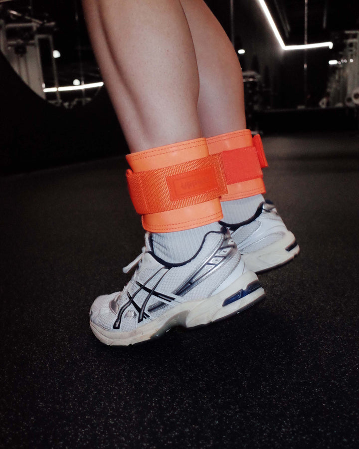 person wearing neon orange uppper ankle weights in gym environment 
