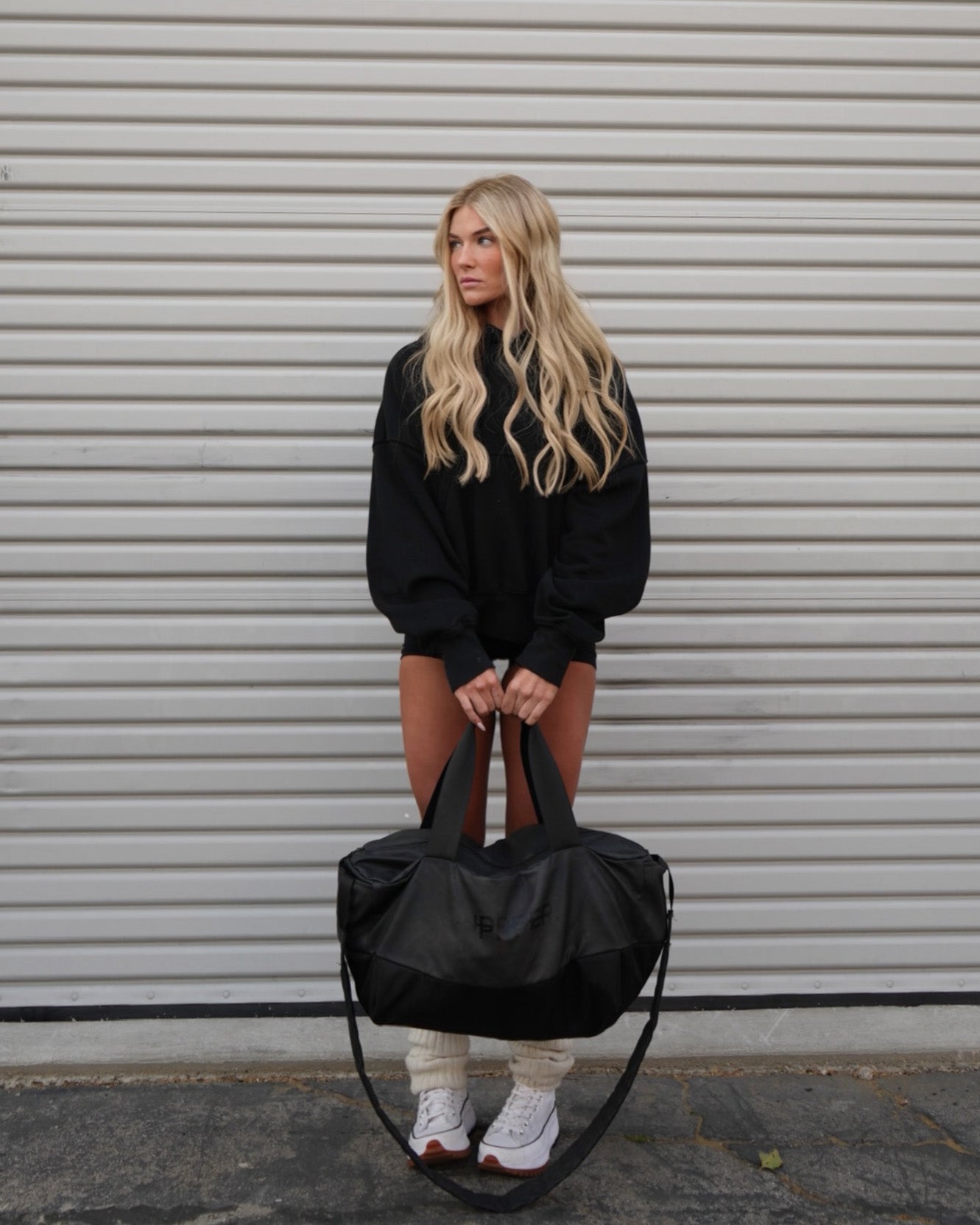 woman holding a black uppper gym bag against a light background