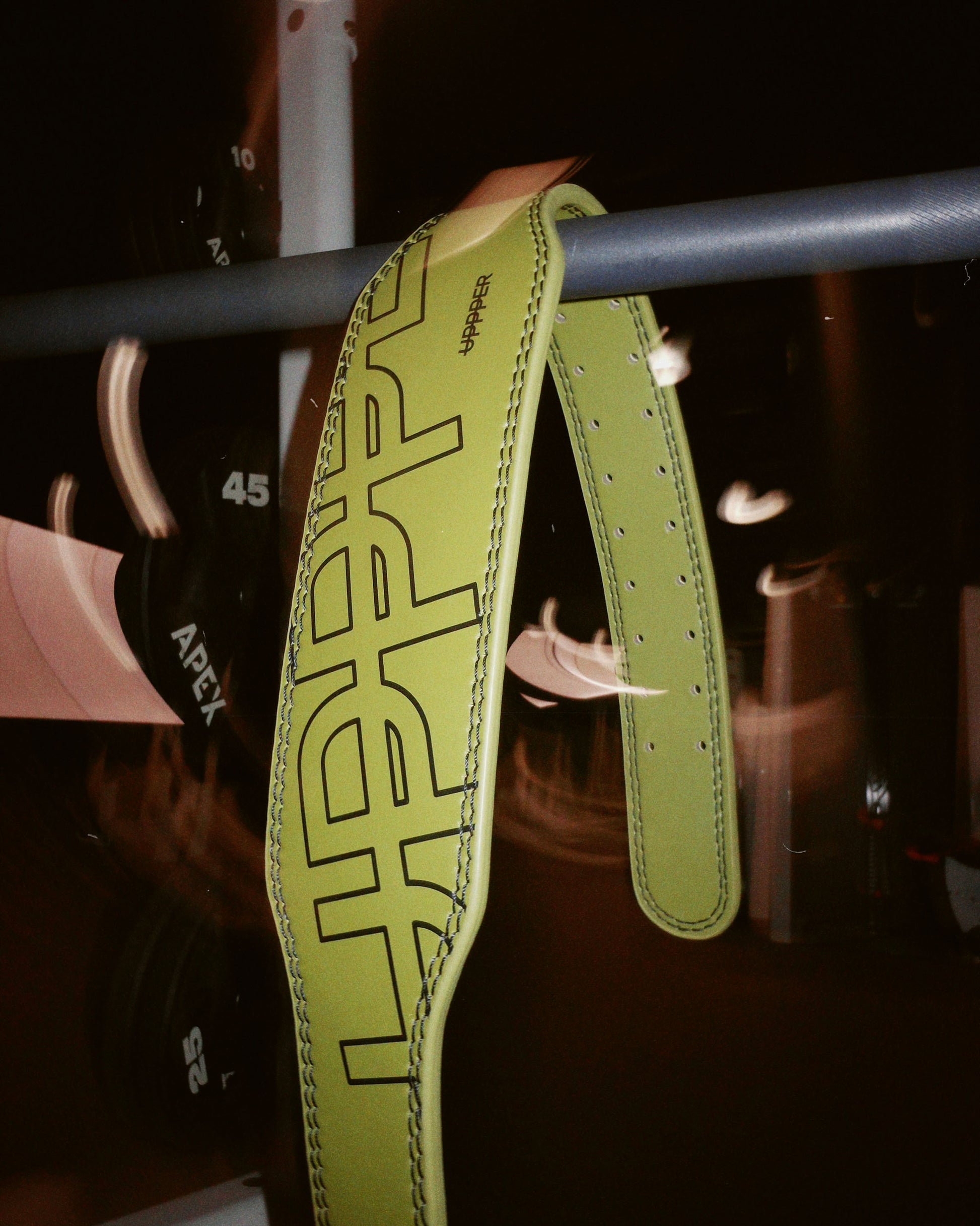 uppper lifting belt in military green color hanging on bar in gym lifestyle shot