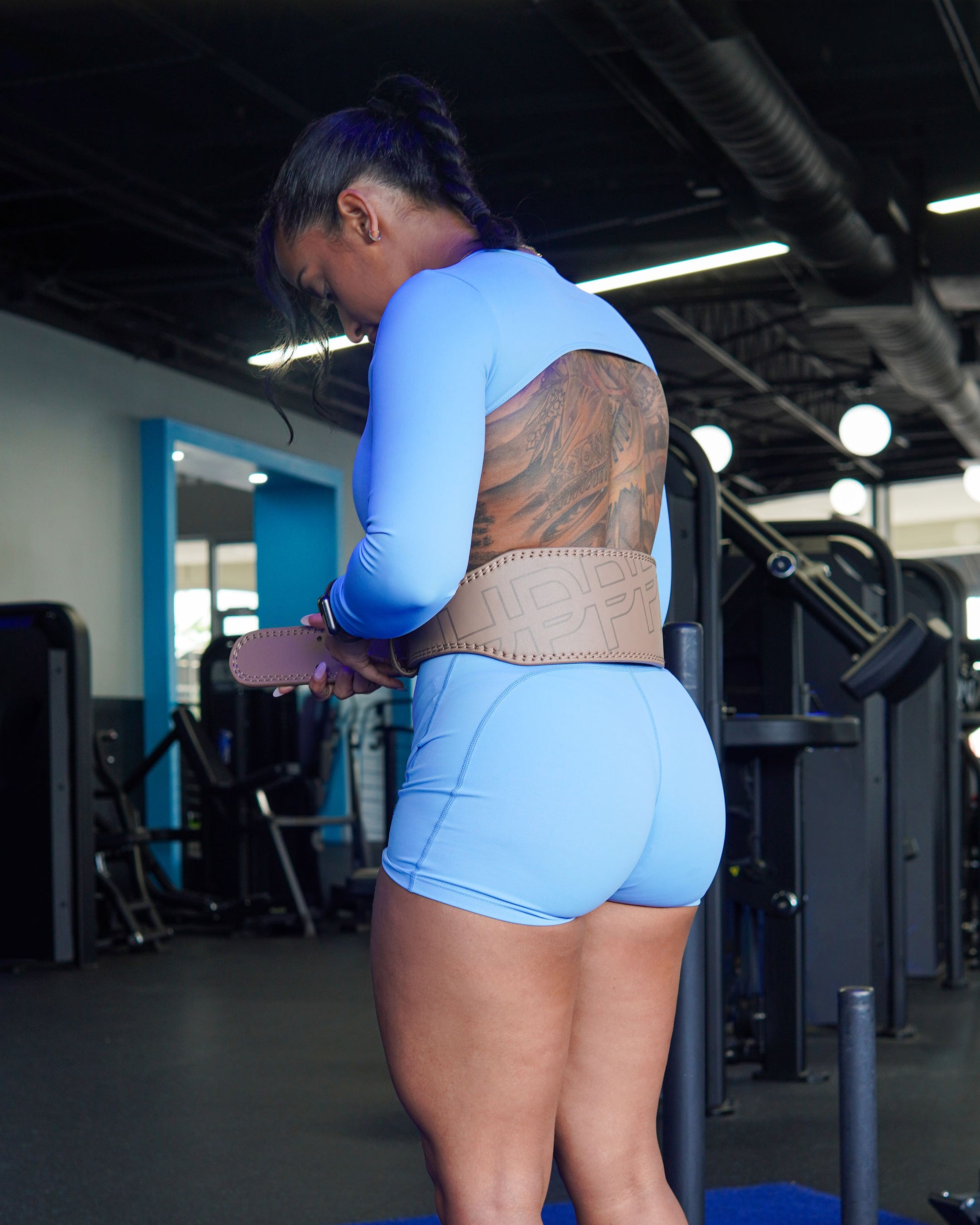 model in gym putting on uppper lifting belt in neutral color