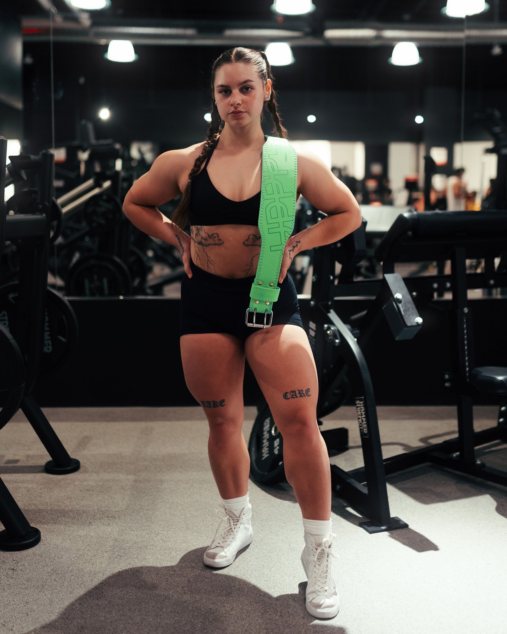 athlete posing in gym with neon green   uppper ifting belt on her shoulder