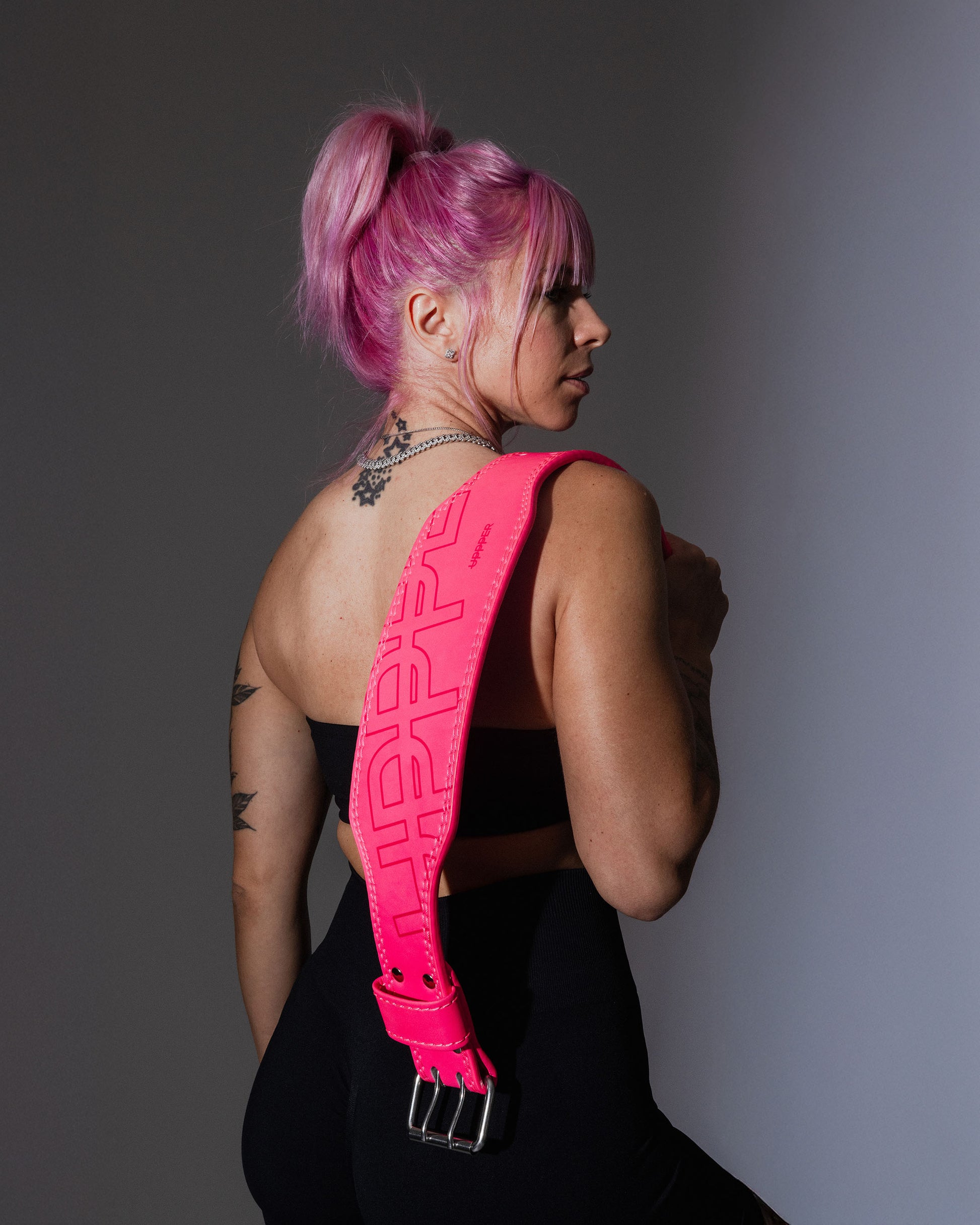 studio shot with grey background model posing with neon pink uppper lifting belt on shoulder