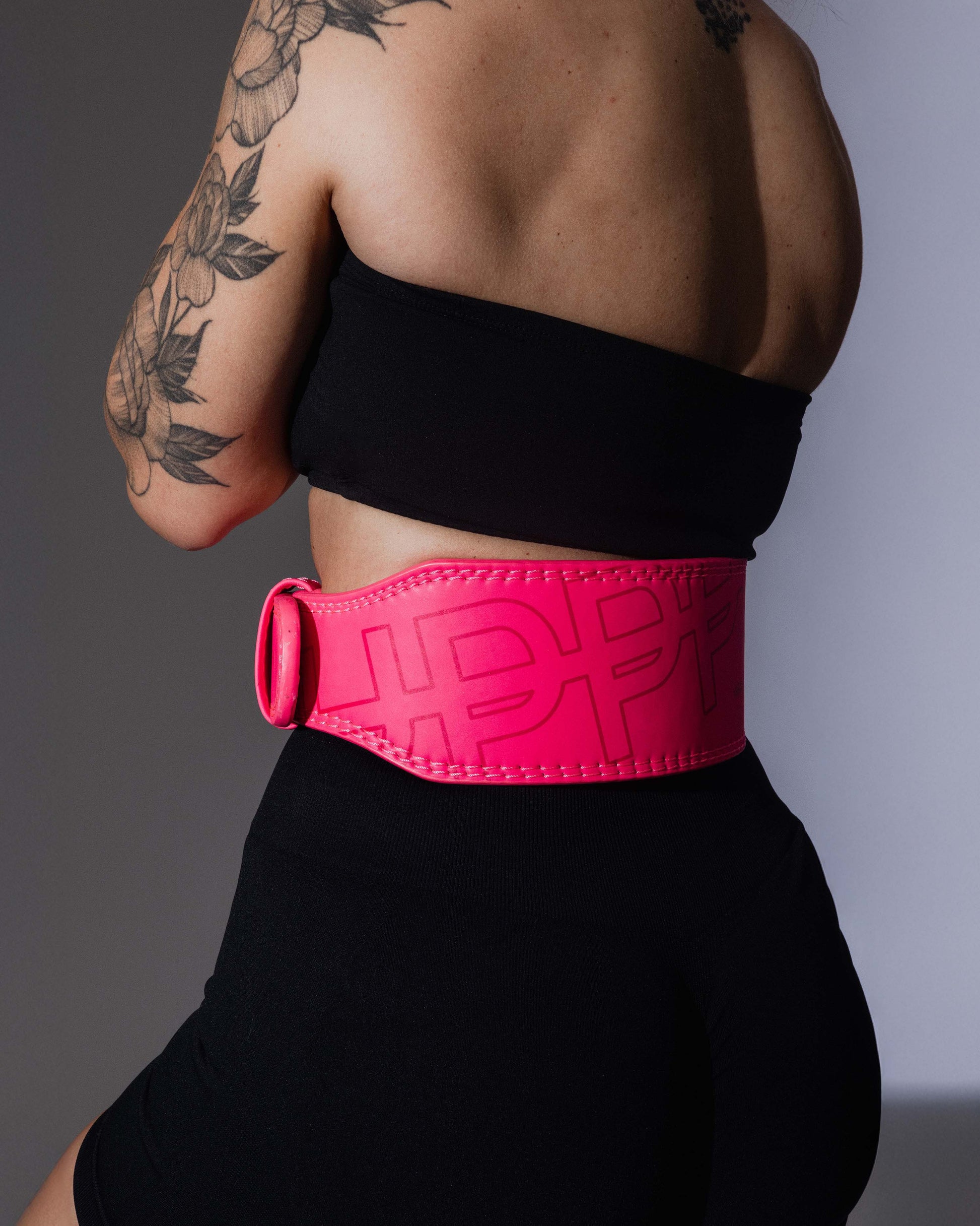 studio shot of model  posing from the back in neon pink uppper lifting belt close-up