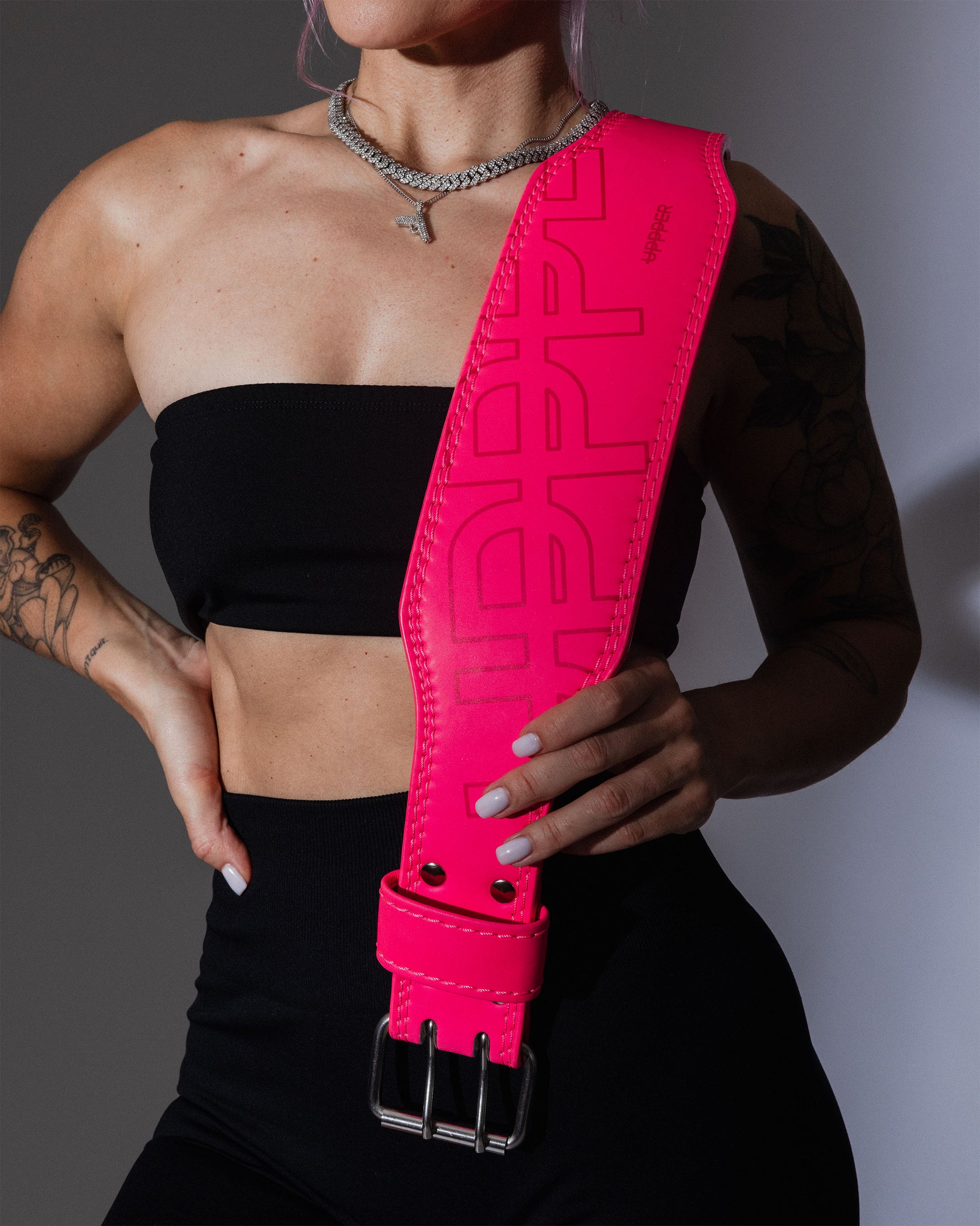 close-up studio shot of neon pink uppper lifting belt hanging from model shoulder showing logo and prong buckle details