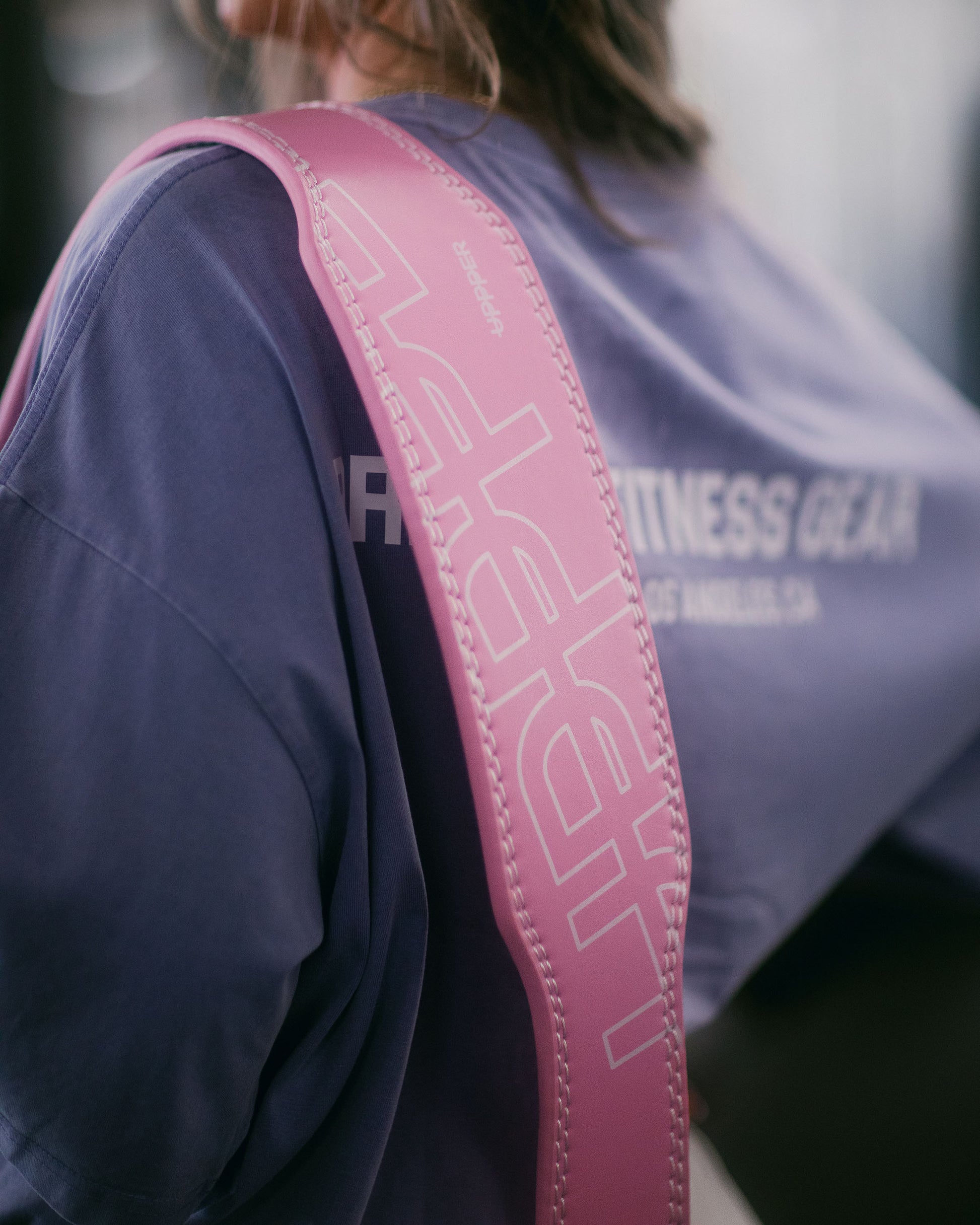 close-up shot of the lifting belt uppper in pink color placed on athlete shoulder showing logo and stitching details 