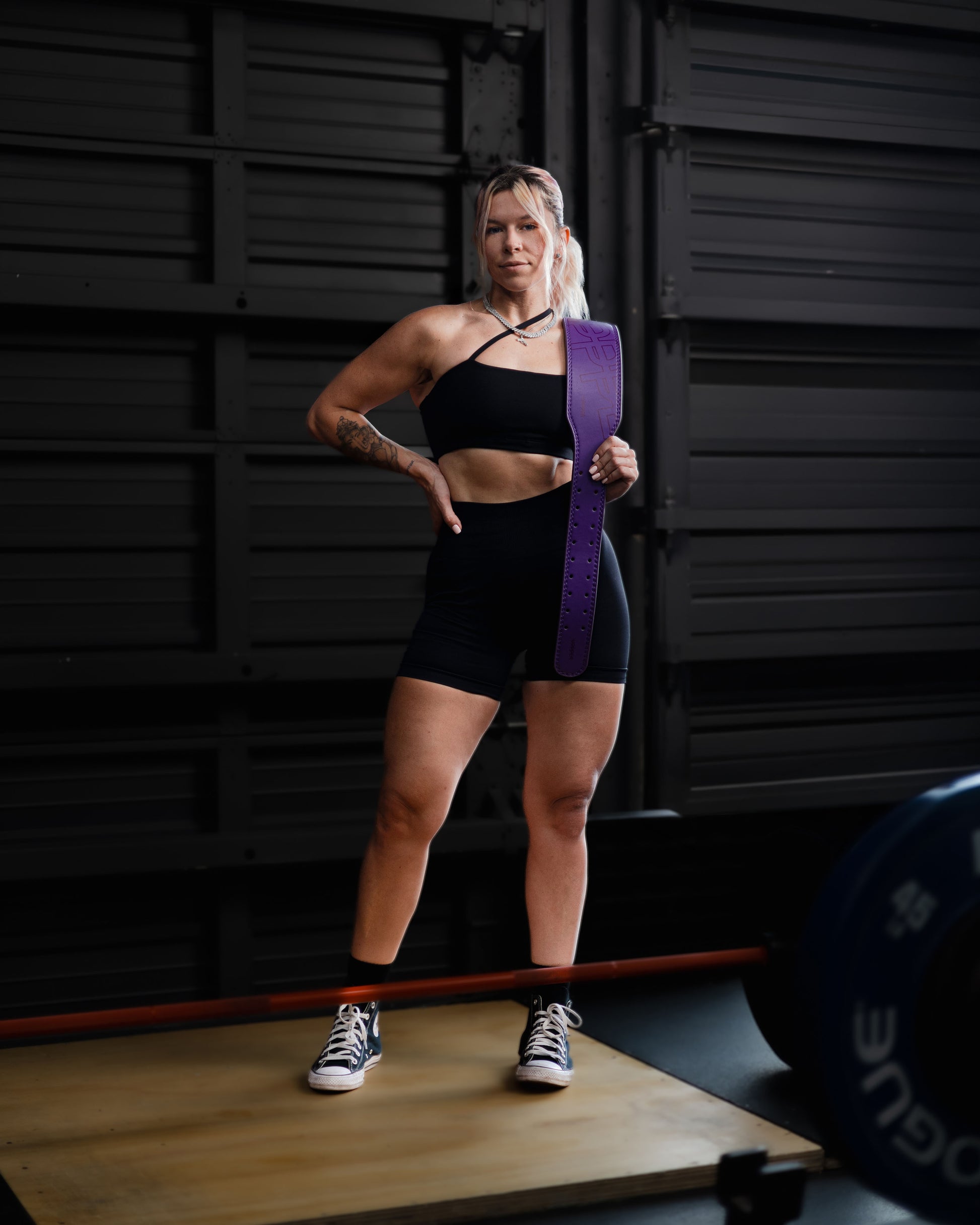 athlete in gym posing with lifting belt uppper in plum color on shoulder 