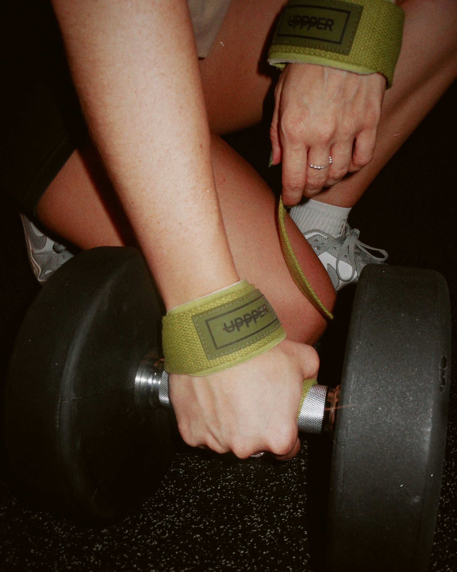 person lifting a weight with khaki uppper lifting wraps on a dark background