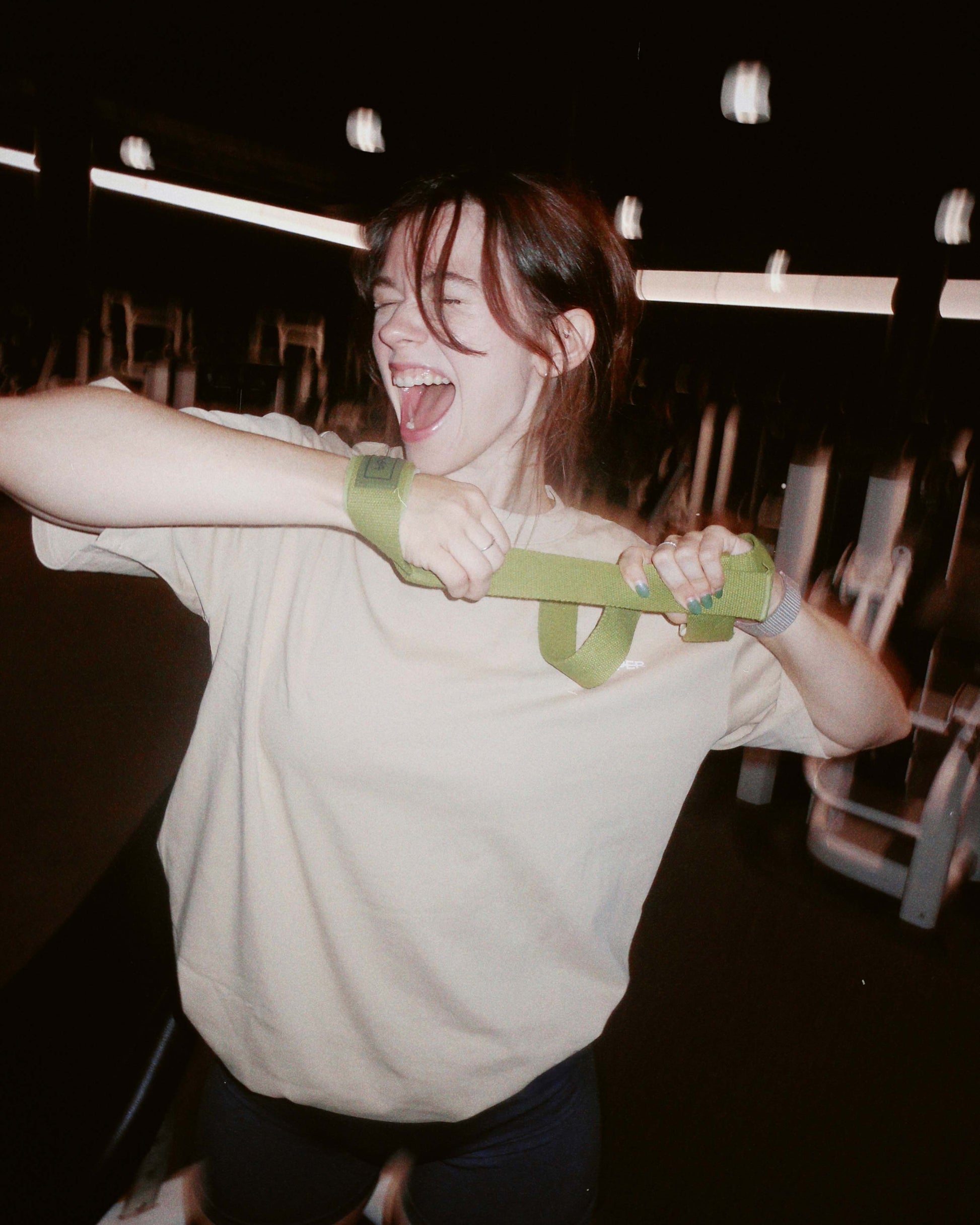 woman exercising with upper lifting straps in green color in a gym setting