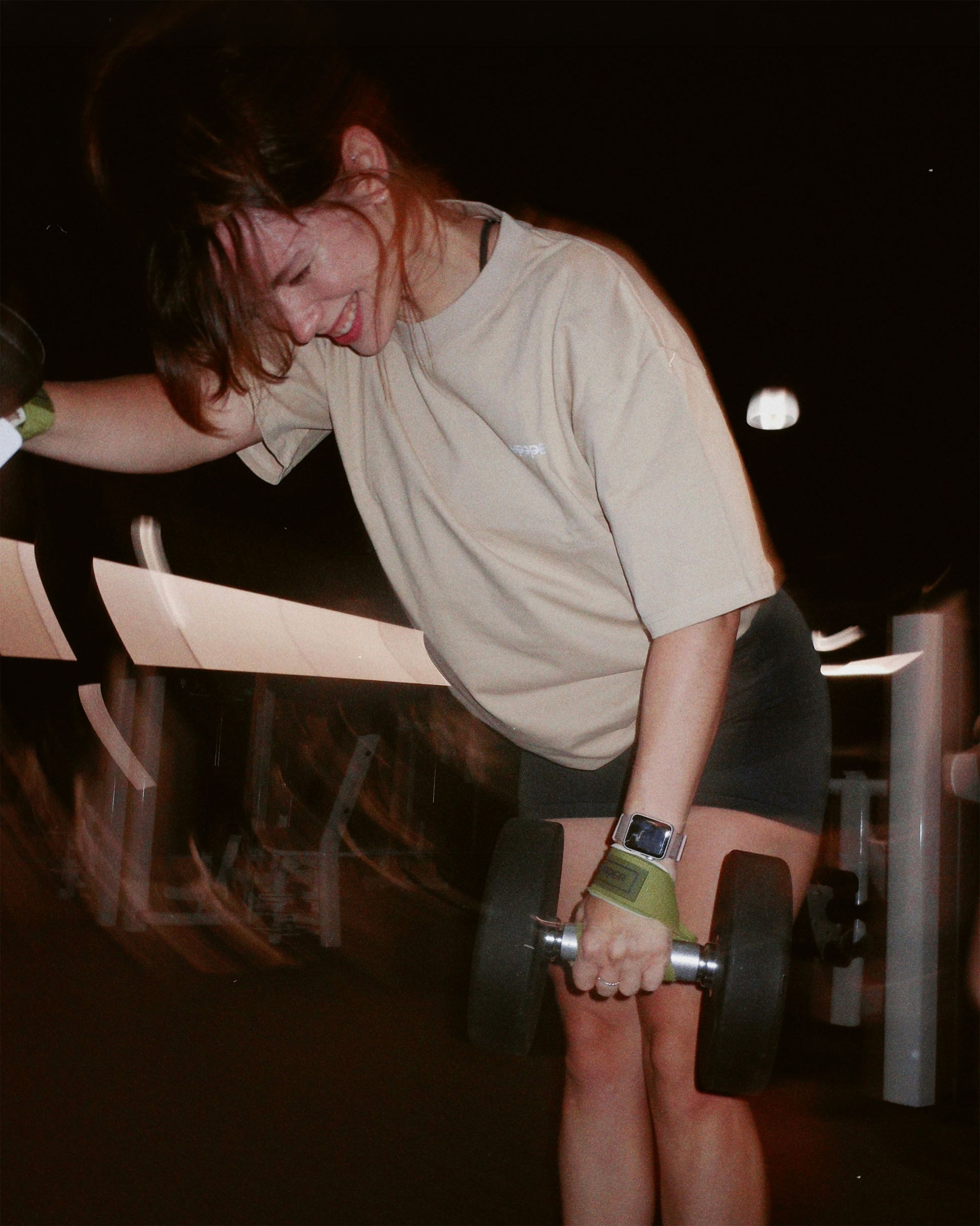 person lifting a dumbbell in a gym setting using uppper lifting straps in khaki color