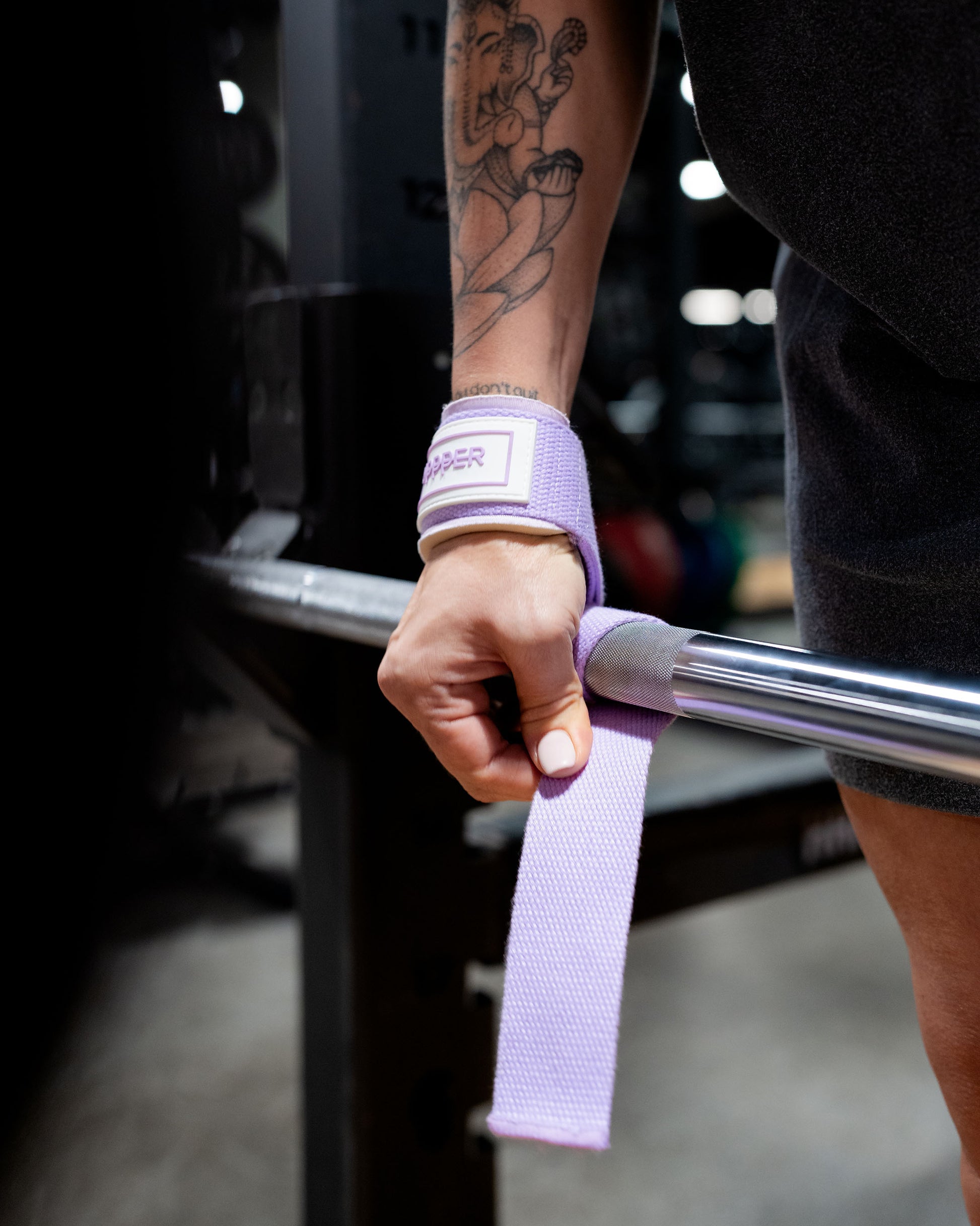 athlete holding a barbell with purple lifting straps showing logo detail in a gym setting